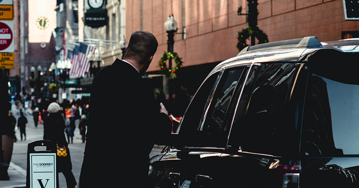 A suited up chauffeur opening the door of a black SUV for you chauffeur vs driver