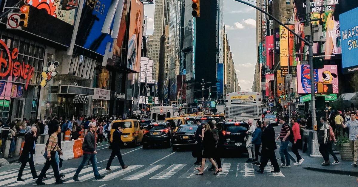 A crowded crosswalk in Times Square, with bumper to bumper traffic behind the pedestrians as chauffeur vs driver face off.